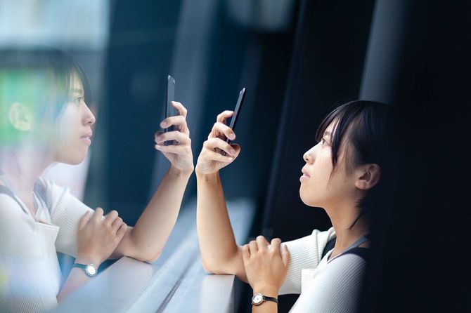 若い女性が窓でスマートフォンを使い、一人で深く考えている