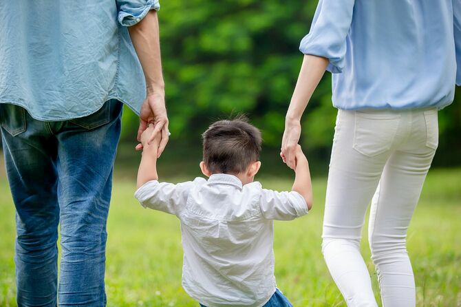 若い両親と子供が手をつないで公園を散歩する