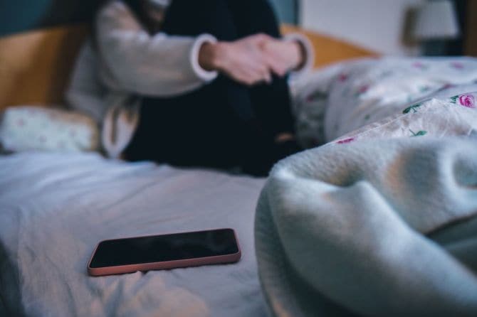 ベッドの上でうずくまりスマートフォンを遠ざけている女の子