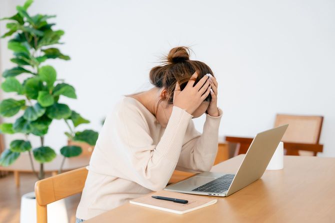 ラップトップで自宅で作業しながら頭を抱える女性
