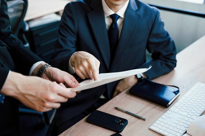 オフィスの机で書類を元に会議をする二人の男の手