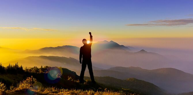日没を迎える山の頂上でガッツポーズをする男性