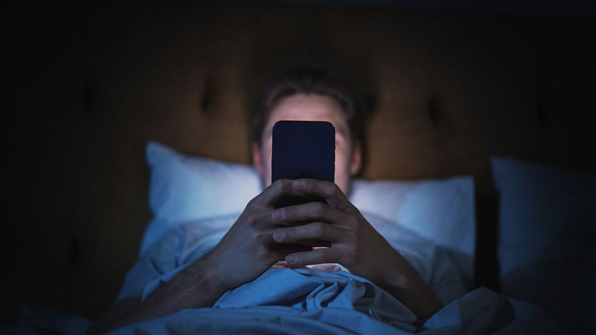 夜に自宅のベッドでスマートフォンを使用する人