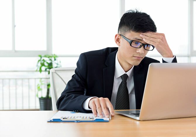 困った顔でパソコンを見ているビジネスマン