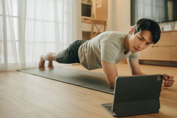 ノートパソコンで動画を見ながらプランクをしている男性