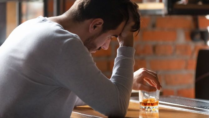 バーでウイスキーのグラスを手に頭を抱えている孤独な男性