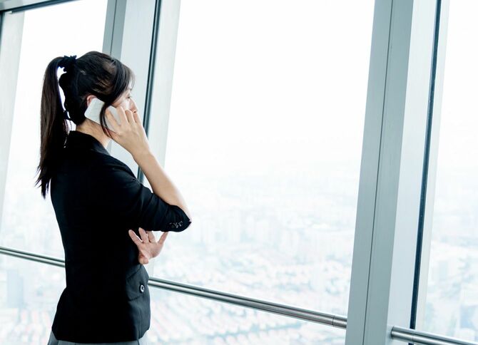 オフィスビルの窓際でスマートフォンを使うビジネスウーマン