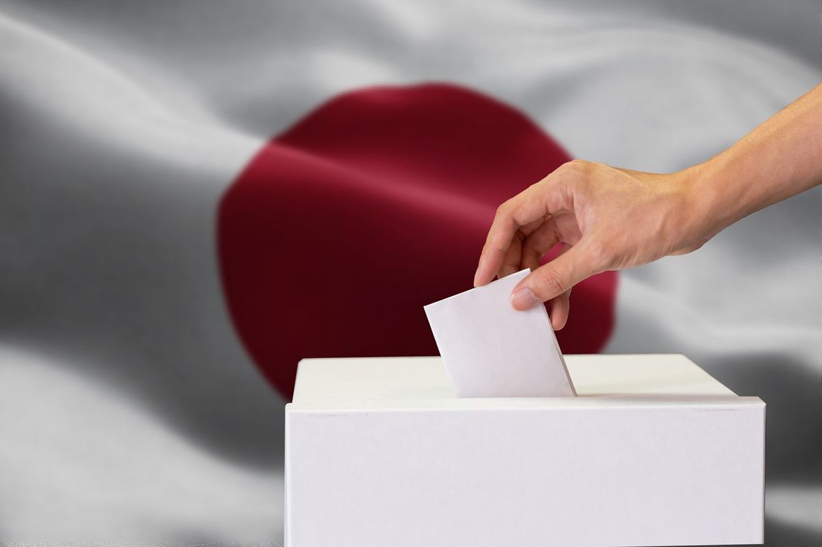 投票箱に一票を投じる人の手元の背景に日章旗