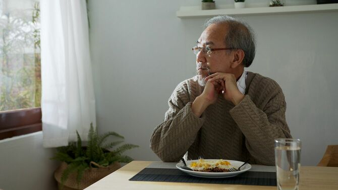 食事中に窓の外を見ている高齢男性