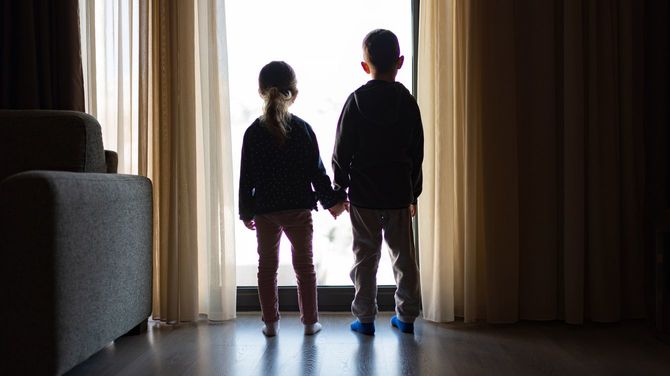 暗い部屋の窓から外を見る2人の子ども