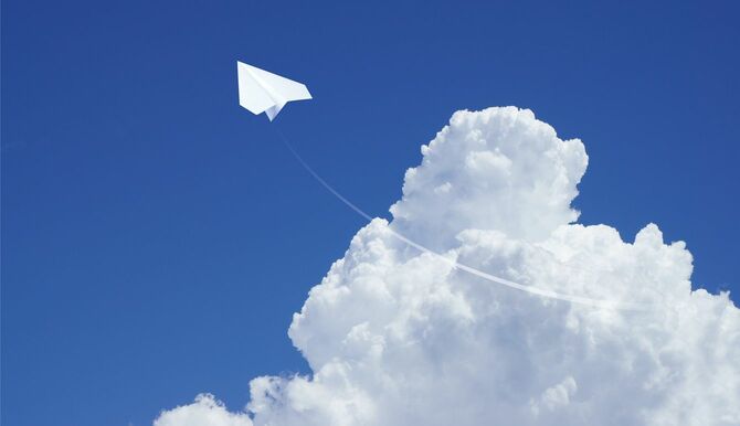 紙飛行機が青空と入道雲をバックに飛んでいく