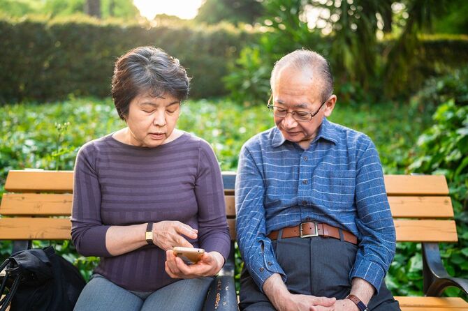 ベンチに座ってスマートフォンを使う年配の夫婦