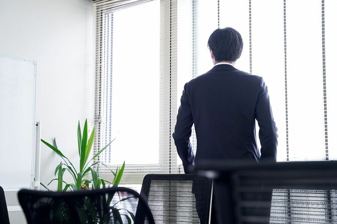 オフィスの窓の外を見ている日本人男性ビジネスマン