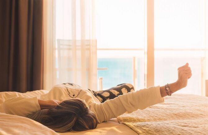 女性は自然な朝の光であふれたホテルの部屋で目を覚ます