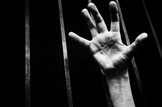 おりに閉じ込められた人の手のイメージ