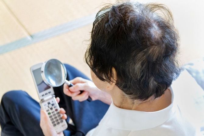 拡大鏡を使用して、携帯メールを読んでいるシニア女性