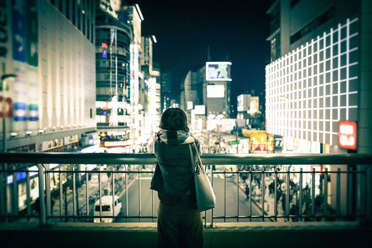 歩道橋の上で一人で夜の街を眺めている女性
