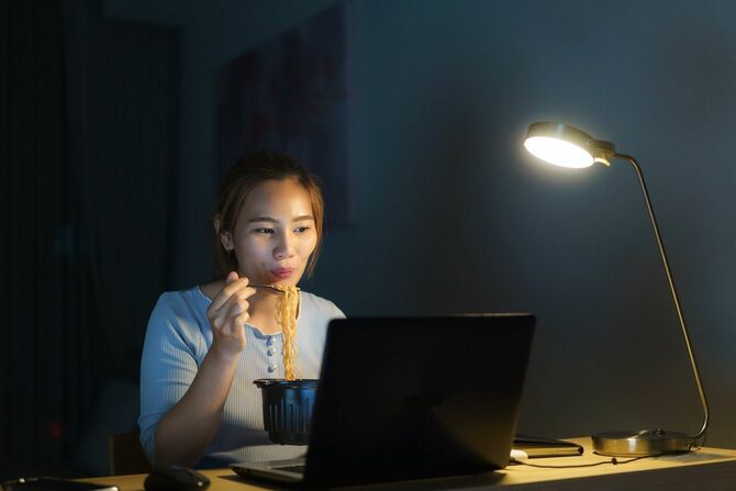 夜にパソコンを見ながらカップラーメンを食べる女性
