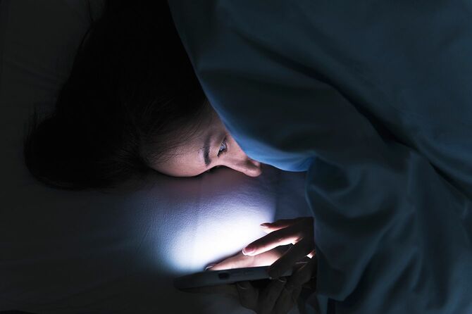 真夜中に暗闇の中でベッドの上にスマートフォンで若い女性のテキストメッセージ