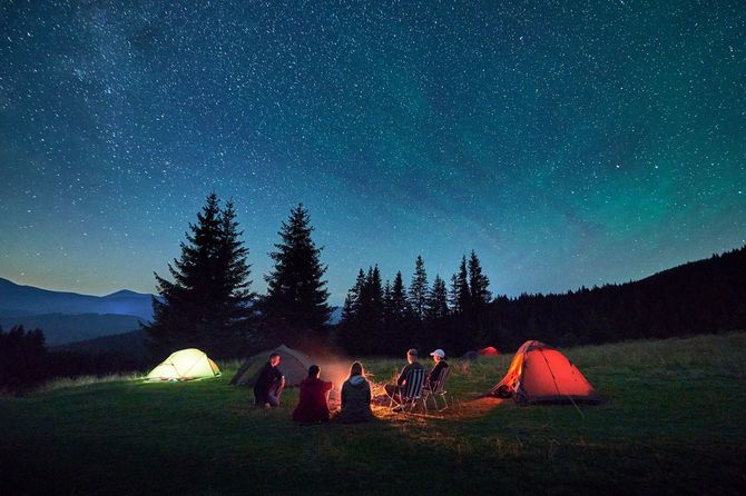 見事な星空の下、焚火を囲んでキャンプしているグループ