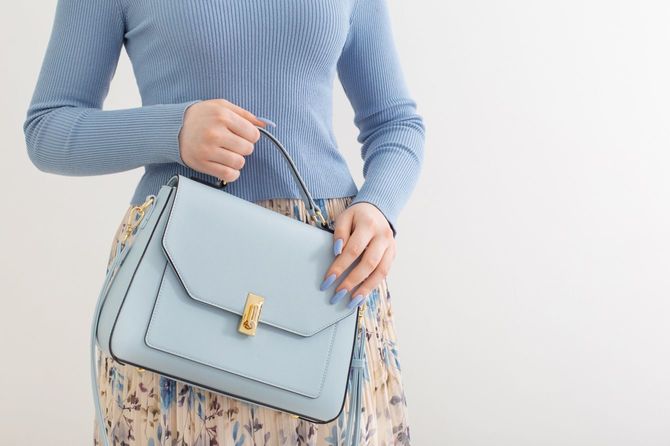ペールブルーのバッグに合わせたニットとネイルの女性