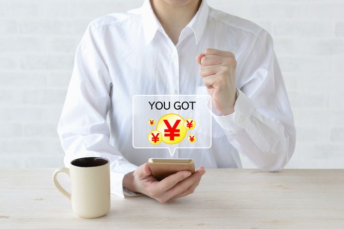 スマートフォンでお金を稼ぎ、ガッツポーズをする女性