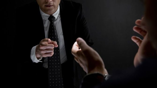 暗い取調室で容疑者を指さす捜査官