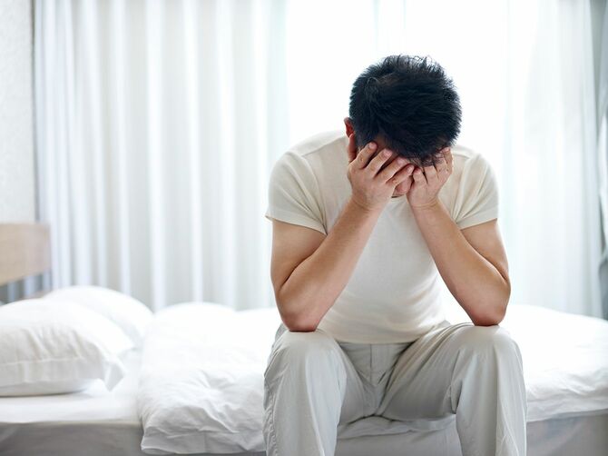 手で顔を覆うベッドの頭の下に座って不眠症に苦しむアジアの男性
