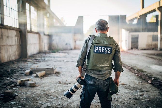 戦闘で屋根がなくなった建物跡に立っている戦場カメラマン