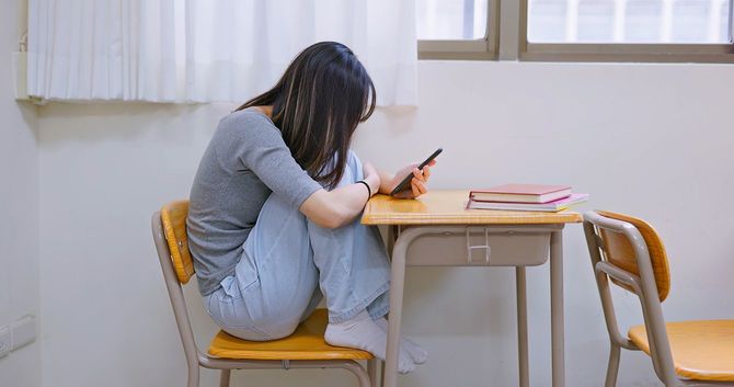 アジアの落ち込んだ女子学生が携帯電話を見て、動揺している