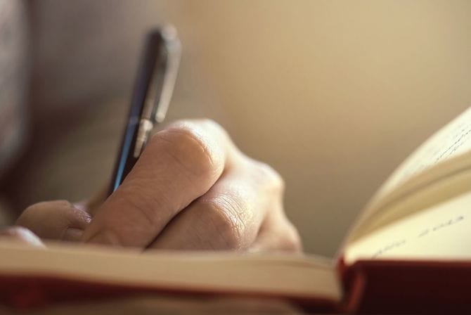本のページにメモを取る女性の手をクローズアップ