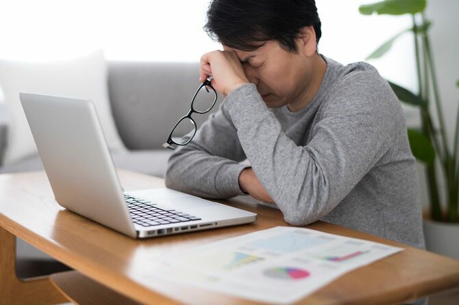 ノートパソコンの前で目の疲れを感じる男性