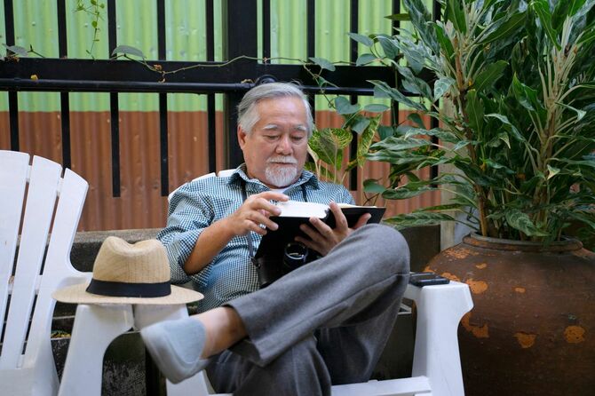 ベランダで読書するシニア男性