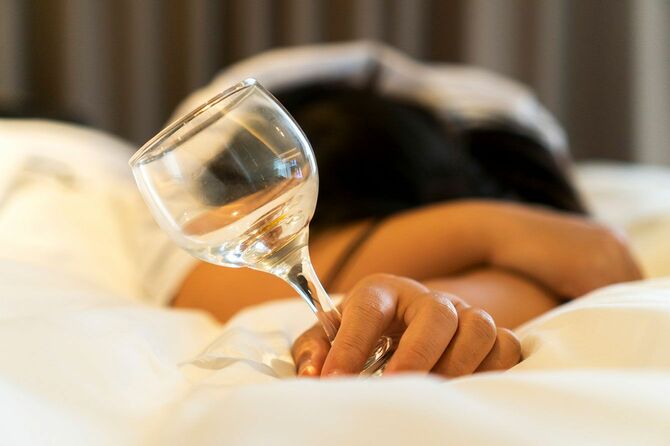ベッドの上でグラスを持ったまま酔いつぶれて寝ている人