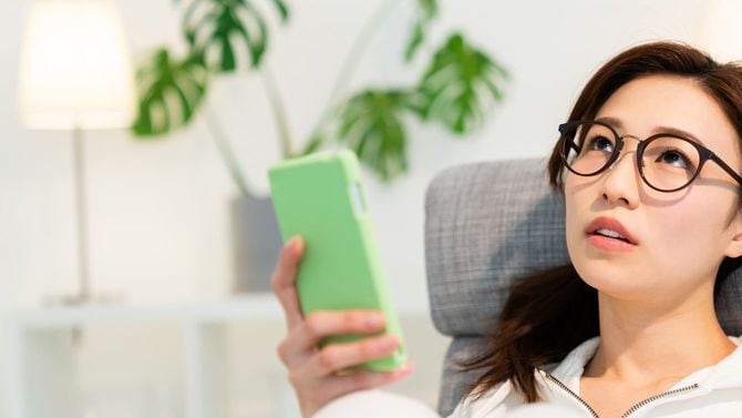 スマホを手に考える女性