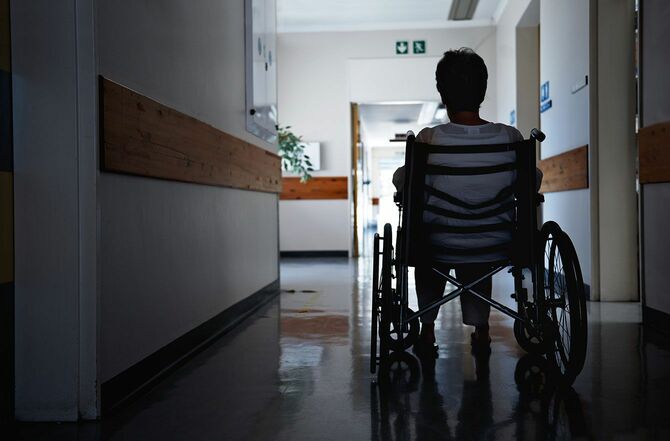 薄暗い病院の廊下で車椅子に座っている高齢女性の後ろ姿