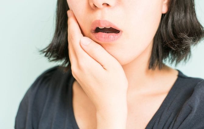歯の痛みを感じて手を当てている女性
