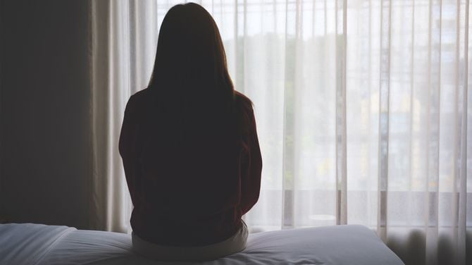 寝室のベッドに一人で座っている女性の後ろ姿