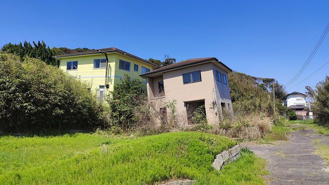 震災の影響による地盤沈下によってひどく傾いた家屋。手前の空き地も波打っているのがわかる。（茨城県鉾田市上幡木）