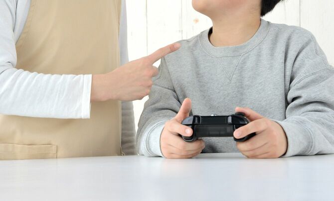 ゲームコントローラーを手に持つ子を叱る母親