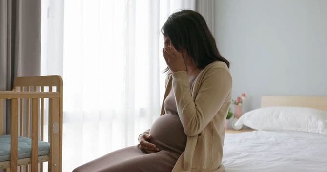 ベッドに腰掛け、泣いている妊婦