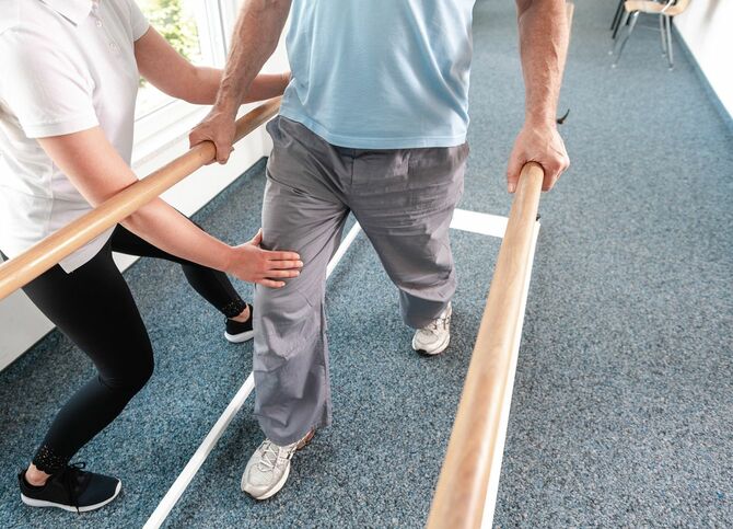 リハビリ中の高齢者が歩くのを手伝う理学療法士