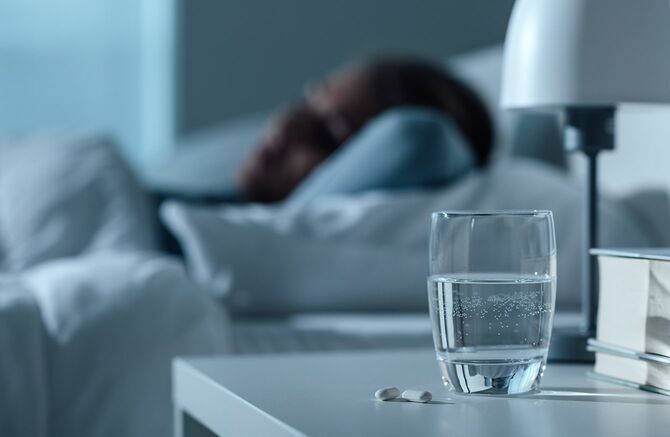 夜、水のガラス、前景、医学と治療コンセプトの丸薬で彼女のベッドで寝ている女性