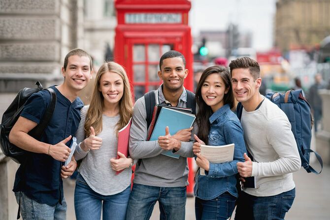 電話ブースの近くで微笑むカメラを見ているロンドンの学生の幸せなグループ