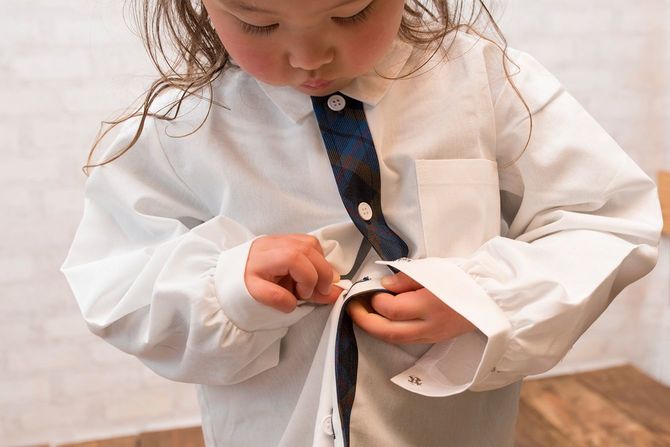 シャツのボタンを押さえようとしている小さな女の子