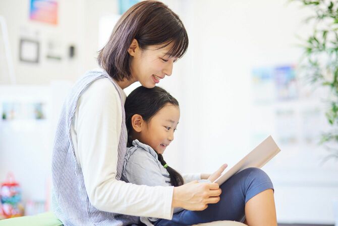 保育園で子どもと絵本を見ている女性