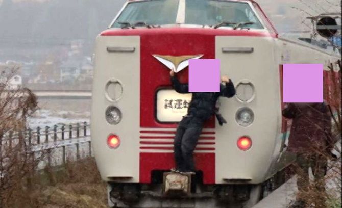 特急「やくも」の連結部分の上でガッツポーズをとる男。肩には大きなレンズを装着したカメラがかかっている