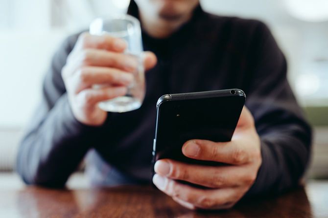 男は水を飲んで、彼の携帯電話をチェックします