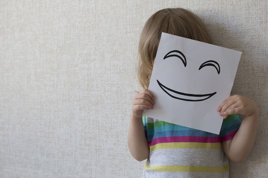 笑った顔が描かれた紙で顔を隠す子ども