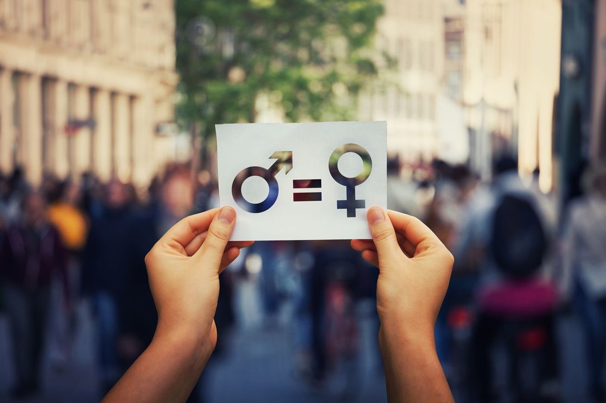 男性記号と女性記号が等号で結ばれた式が描かれたカードを路上で持つ人